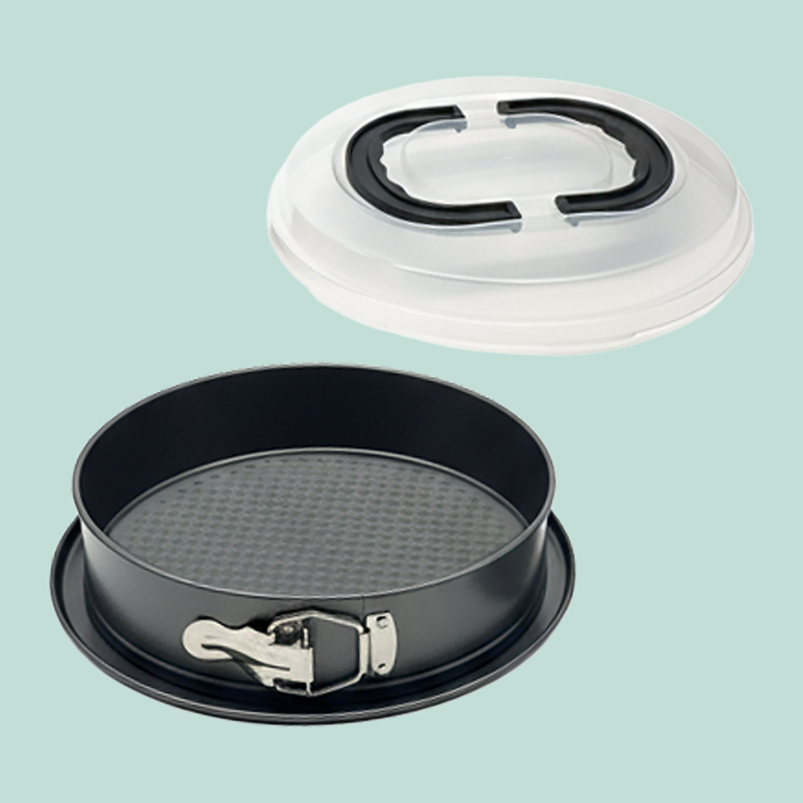 Eine dunkelgraue, runde Springform mit Verschluss und passendem weißem Plastikdeckel mit schwarzem Griff auf hellgrünem Grund.