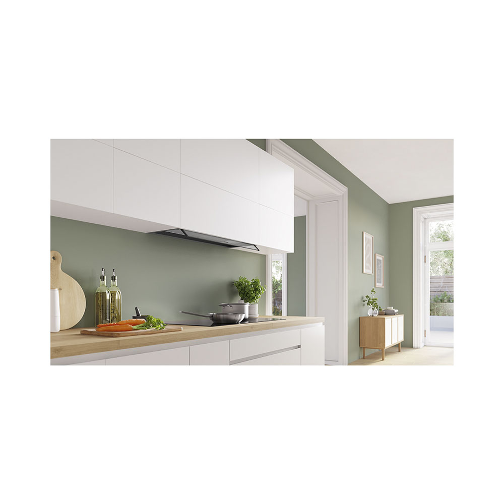 Cucina moderna con pensili bianchi, pareti verdi, piano di lavoro in legno, piano cottura con padella e tagliere con verdure.