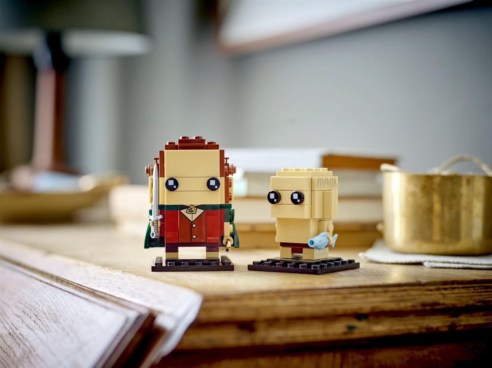 Zwei Lego BrickHeadz Figuren, Aragorn mit Schwert und Gollum mit Fisch, stehen auf einem Holztisch in einem Raum.