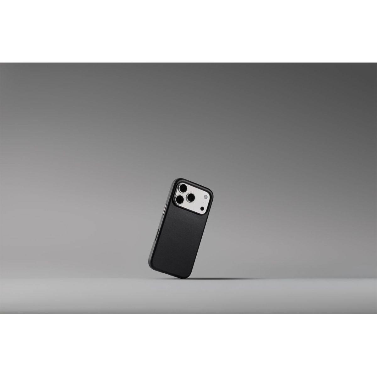 Uno smartphone nero con tripla fotocamera si trova in diagonale su una superficie grigia su sfondo grigio.