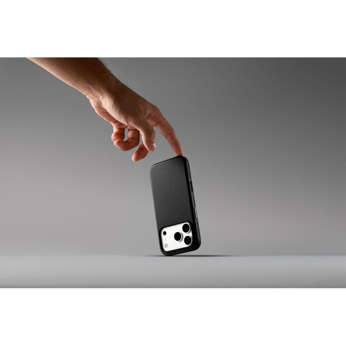 Una mano tocca delicatamente uno smartphone nero in piedi su una superficie grigia.
