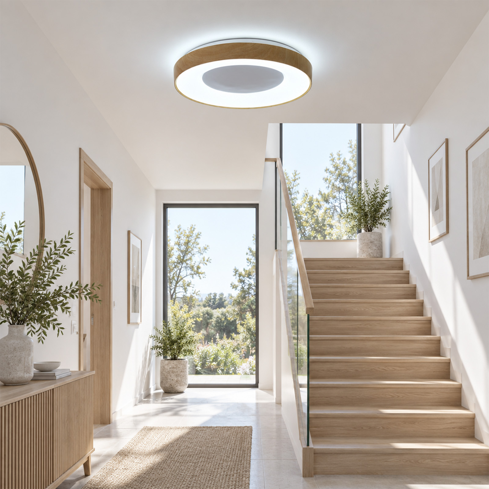 Pasillo luminoso con paredes blancas, escaleras de madera, lámpara de techo redonda y plantas en macetas.