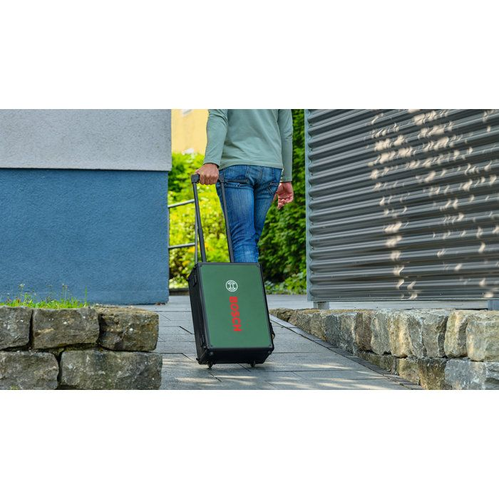 Eine Person zieht einen grünen Bosch-Werkzeugkasten auf Rädern über einen gepflasterten Weg.