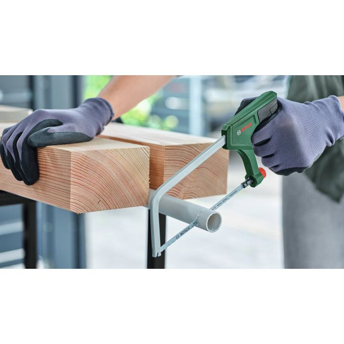 Person sägt mit einer grünen Bosch-Handsäge ein graues Rohr zwischen Holzträgern ab.