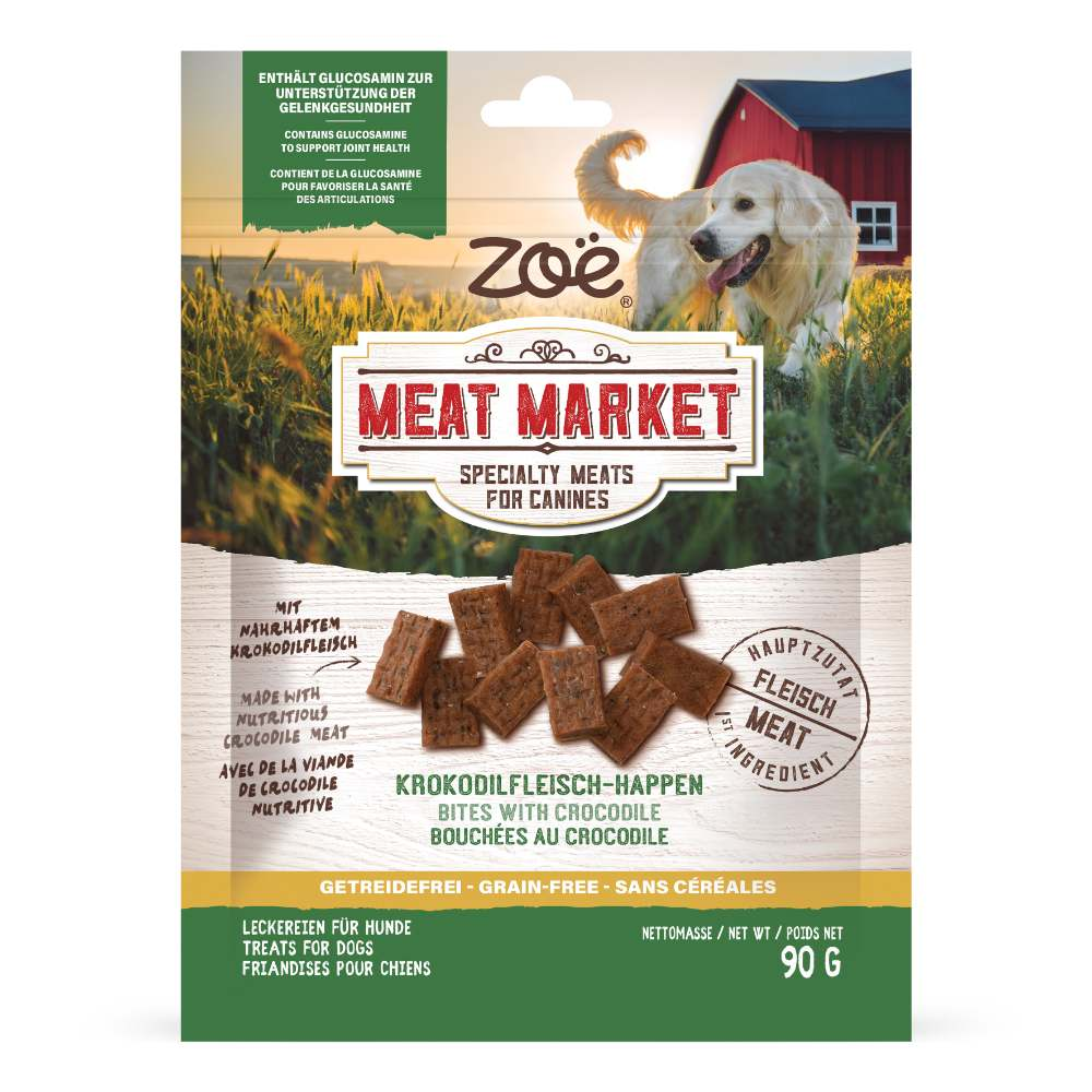 Envase de golosinas para perros de carne de cocodrilo Zoë Meat Market con golden retrievers frente a un granero.