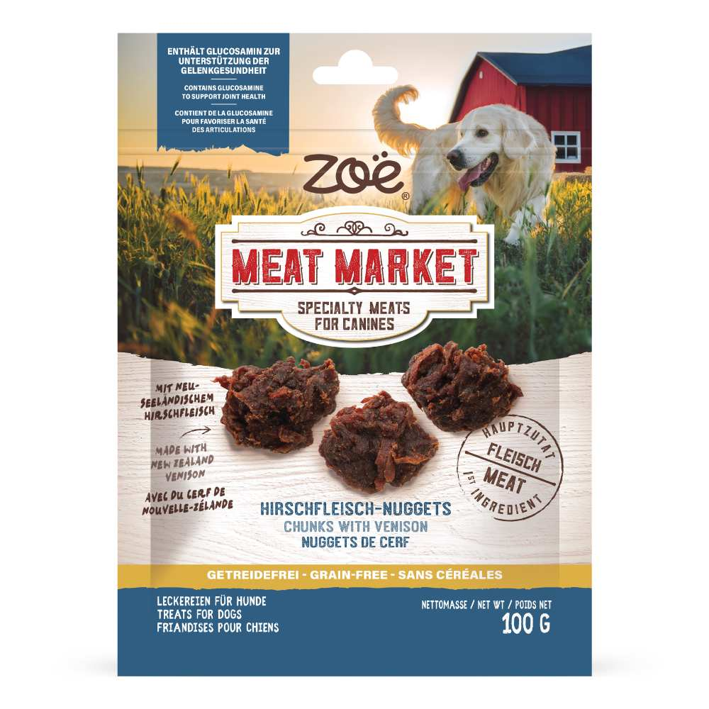 Empaque de golosinas de veniste para perros Zoe Meat Market con un golden retriever y tres trozos de carne en un campo.