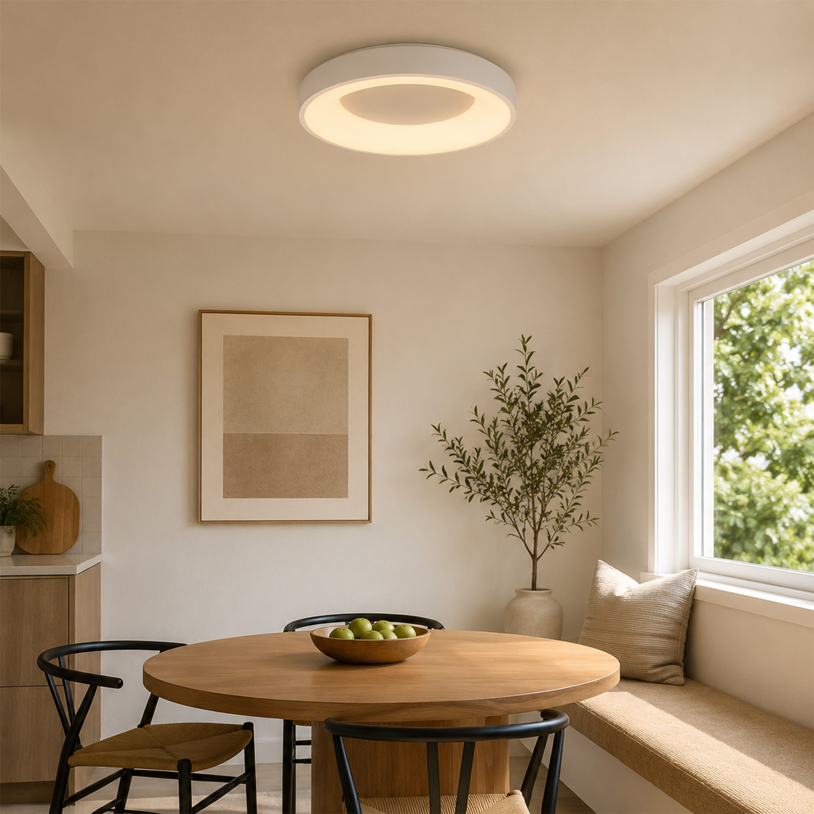 Un comedor luminoso con mesa redonda de madera, sillas negras, frutero, arte enmarcado y banco con cojín.
