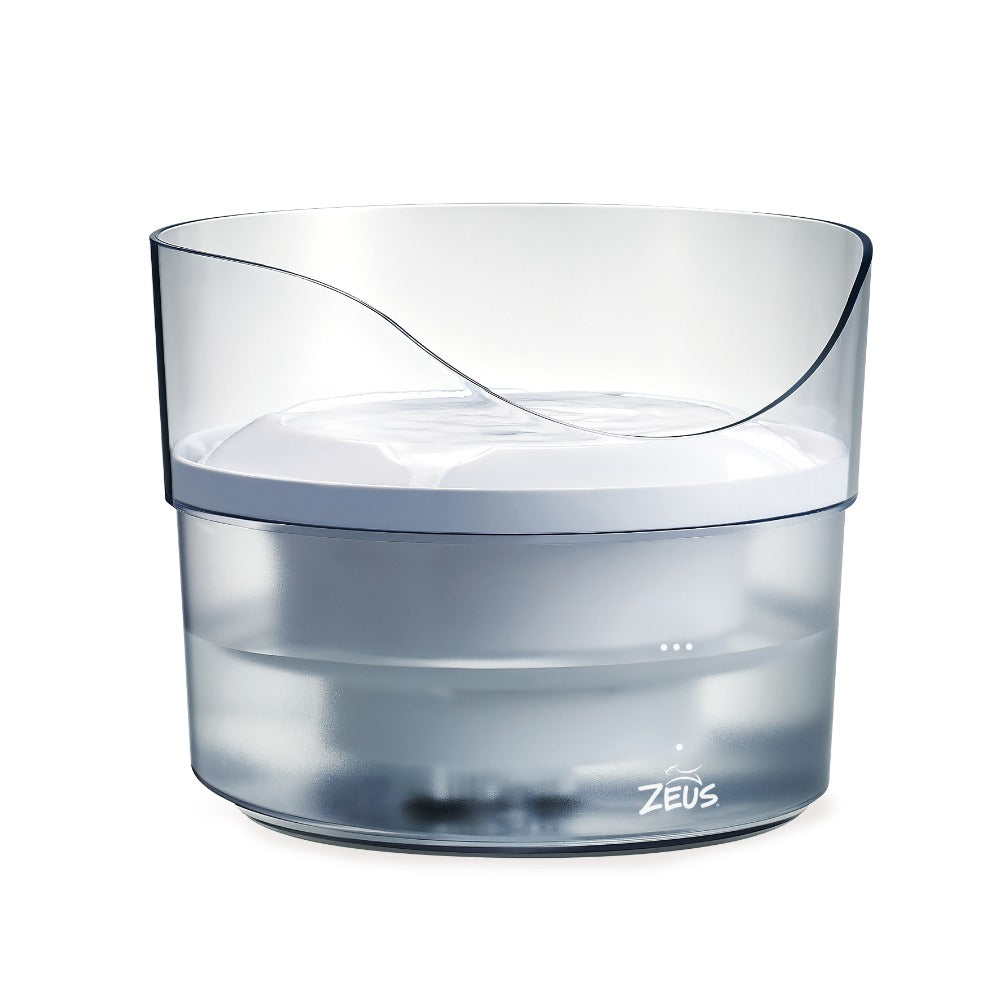 Una fuente para mascotas Zeus de plástico transparente con parte superior blanca y nivel de agua visible, sobre fondo blanco.