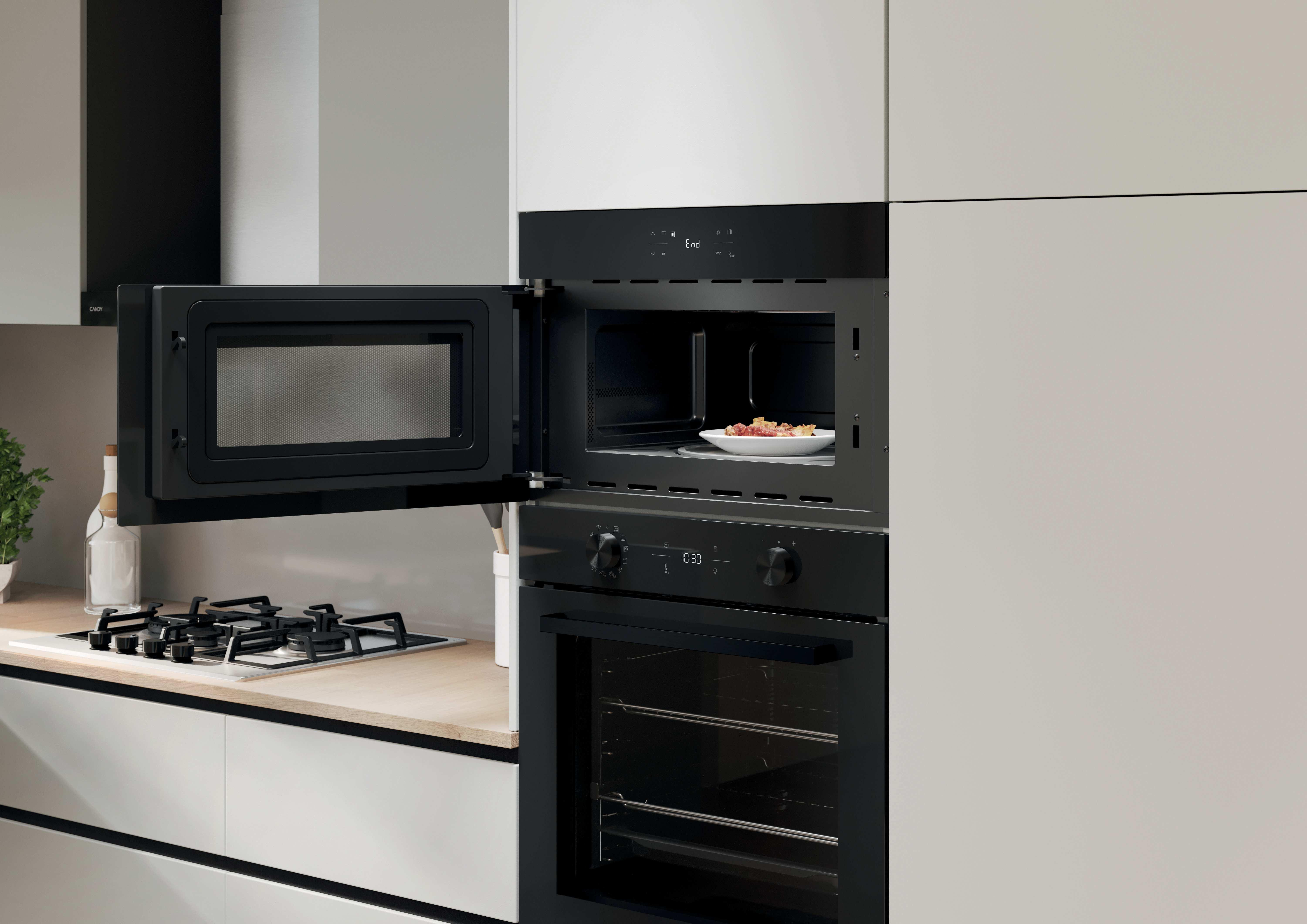 Cucina moderna con microonde incassato, forno e piano cottura a gas su piano di lavoro in legno chiaro.