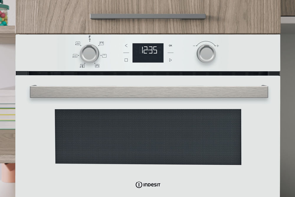 Un forno da incasso Indesit bianco con due manopole argentate, un display digitale e una grande maniglia.