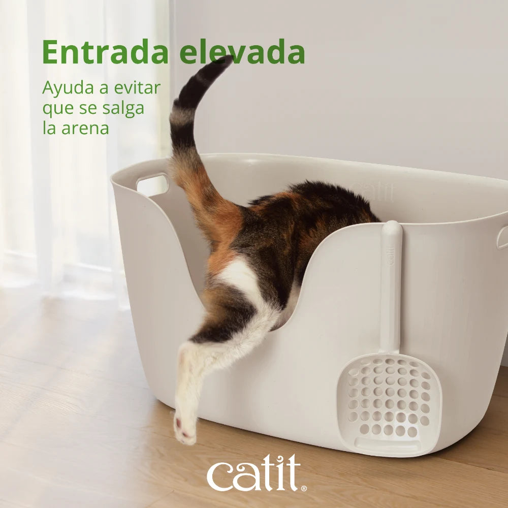 Un gato calicó entra en un arenero blanco con una pala adjunta.