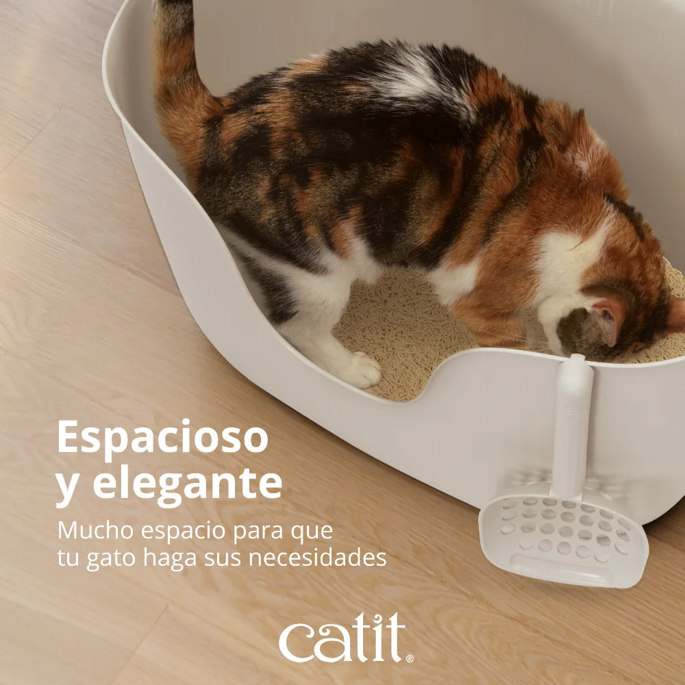 Un gato calicó está dentro de una caja de arena blanca y grande con pala.