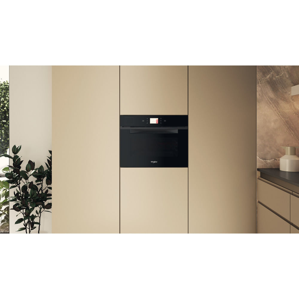 Un forno a incasso nero in una cucina beige con una pianta a sinistra e una caffettiera a destra.