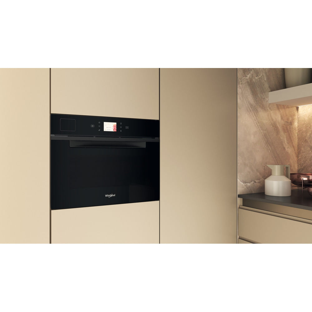 Un forno da incasso Whirlpool nero integrato in eleganti mobili da cucina beige con paraschizzi in marmo.