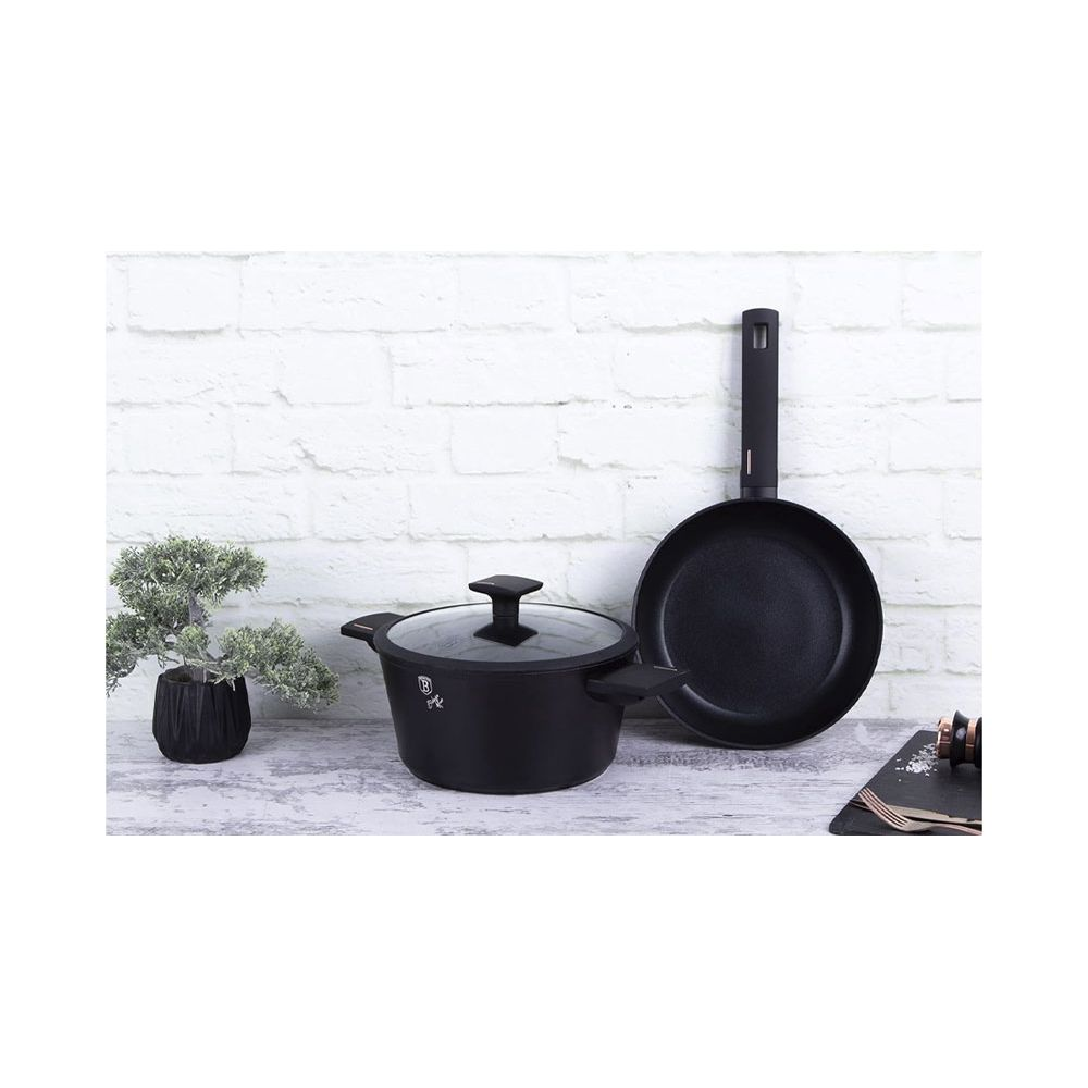 Casseroles et poêle noires devant un mur de briques blanches avec une petite plante.