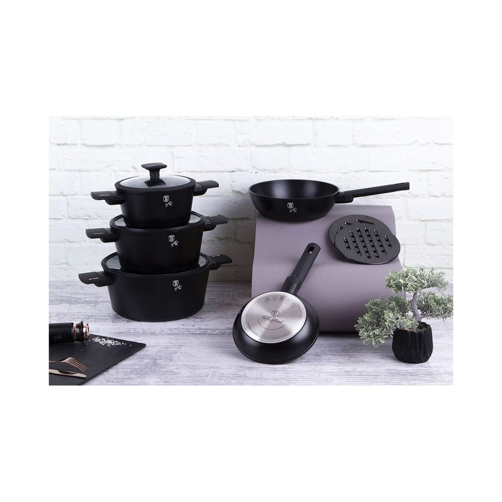 Un ensemble de casseroles et poêles noires sur fond de brique blanche avec plante.