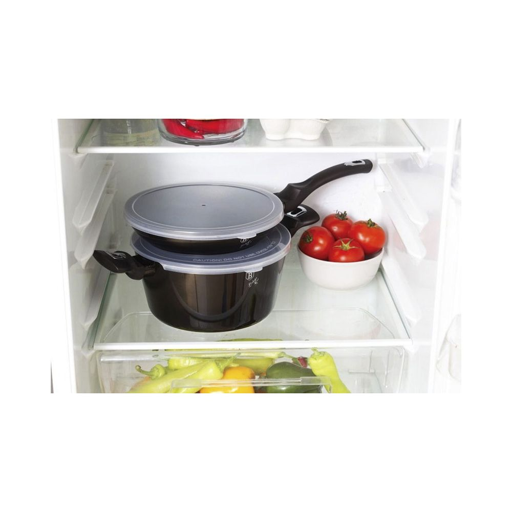 Une étagère de réfrigérateur avec des casseroles noires, un bol de tomates et des légumes frais.