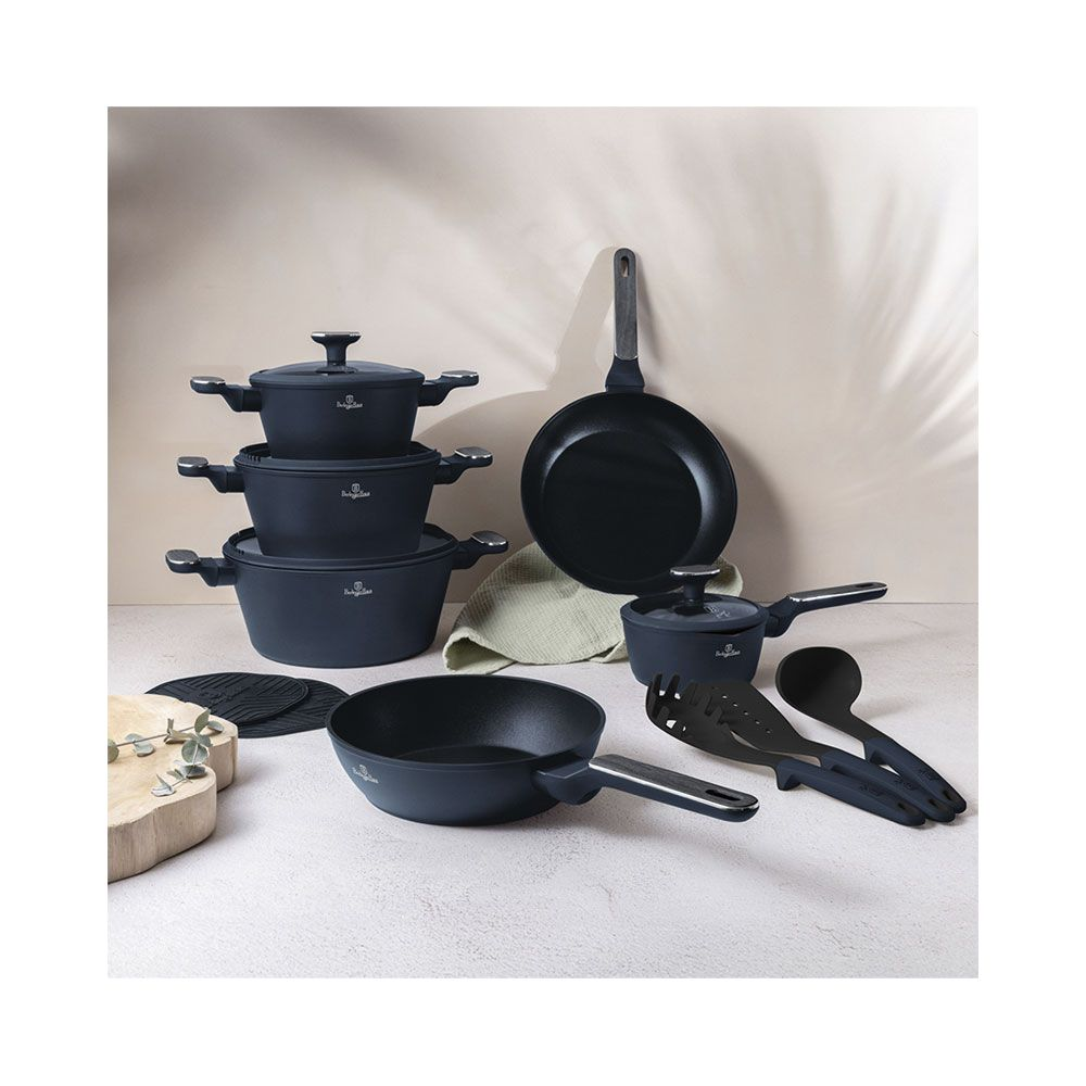 Un ensemble de casseroles, poêles et ustensiles de cuisine bleu foncé sur une table devant un mur neutre.