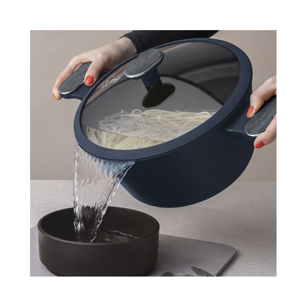 Personne versant l'eau d'une casserole bleu foncé contenant des pâtes dans un bol.