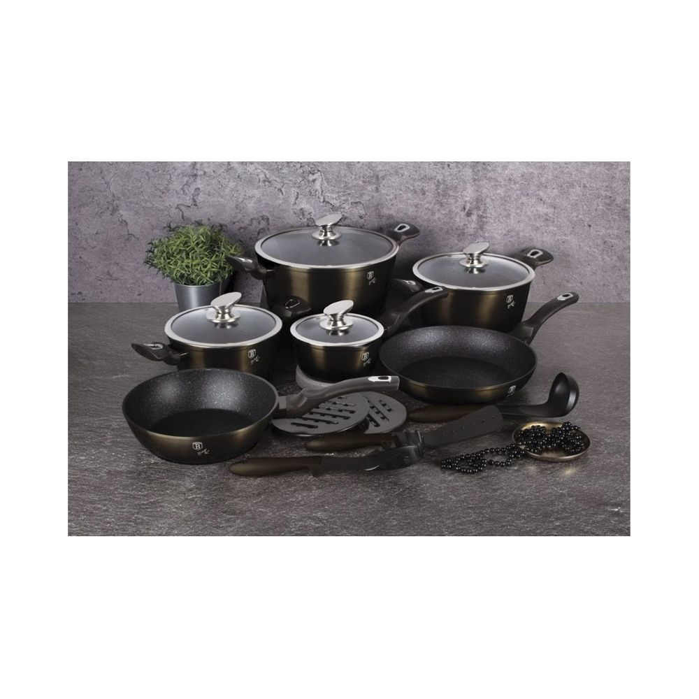 Un ensemble de casseroles et poêles métalliques foncées avec couvercles en verre, ustensiles et petite plante sur un plan de travail.