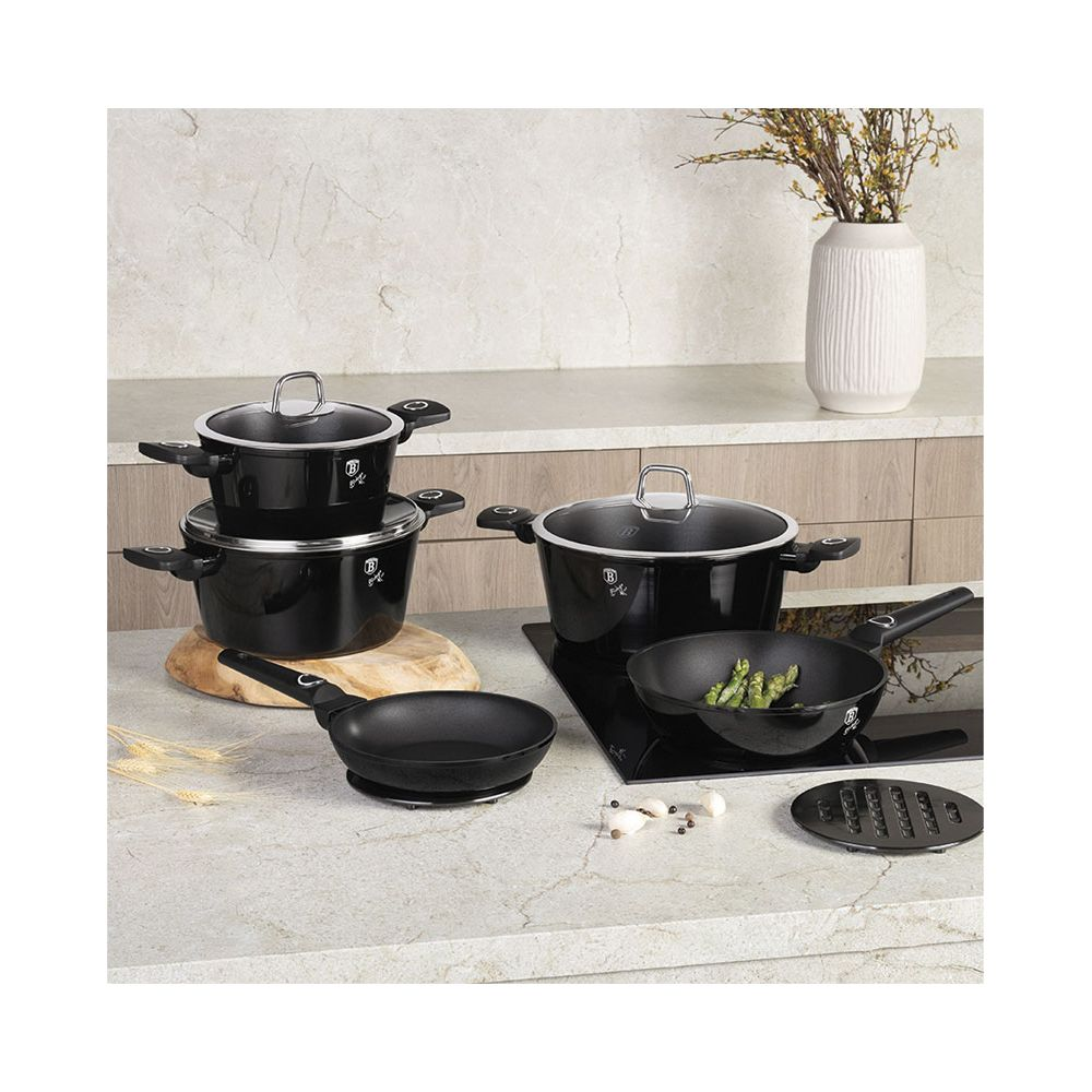 Un ensemble d'ustensiles de cuisine noirs, casseroles, poêles et couvercles, sur un plan de travail.