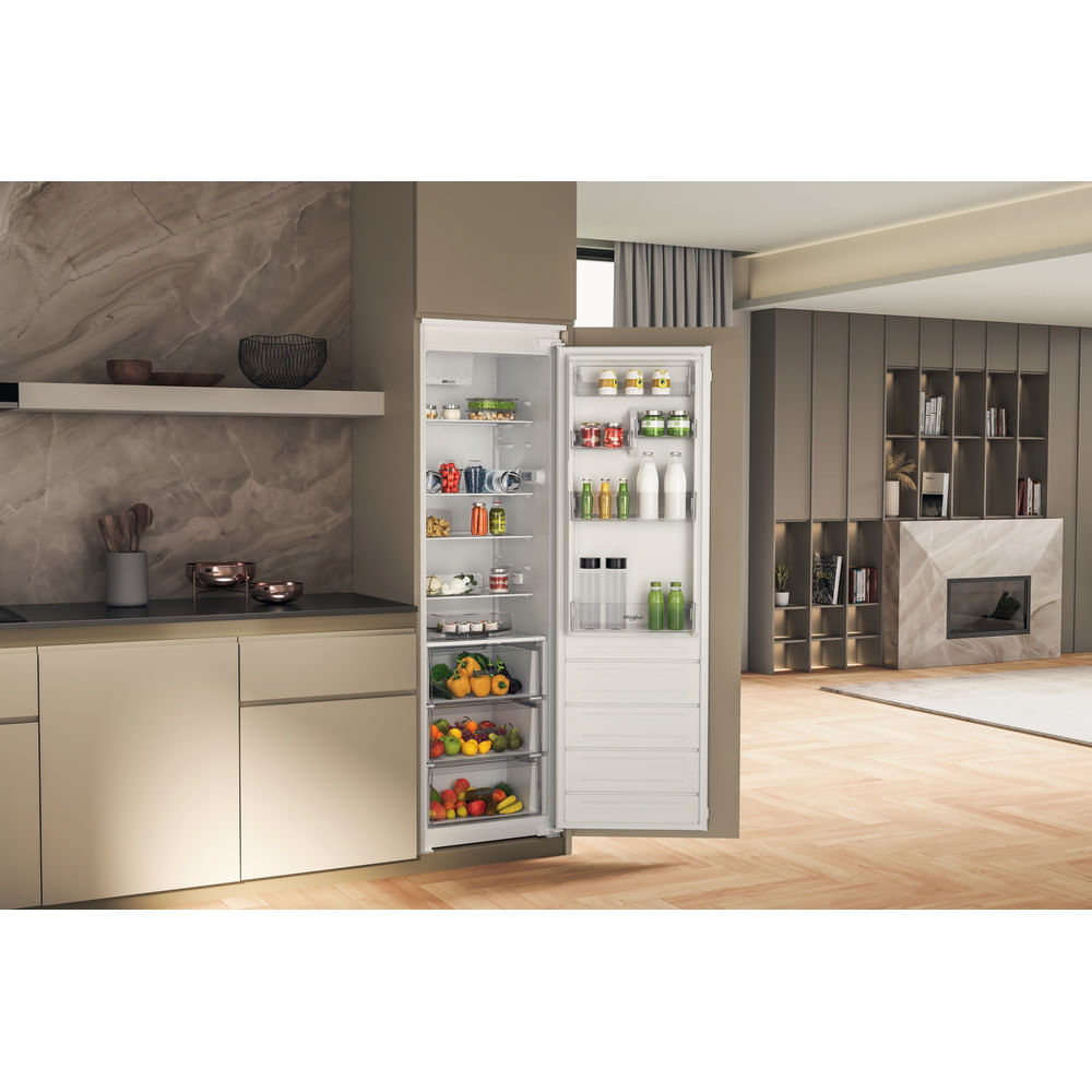 Un frigorifero da incasso bianco aperto pieno di cibo si trova in una cucina moderna ed elegante.