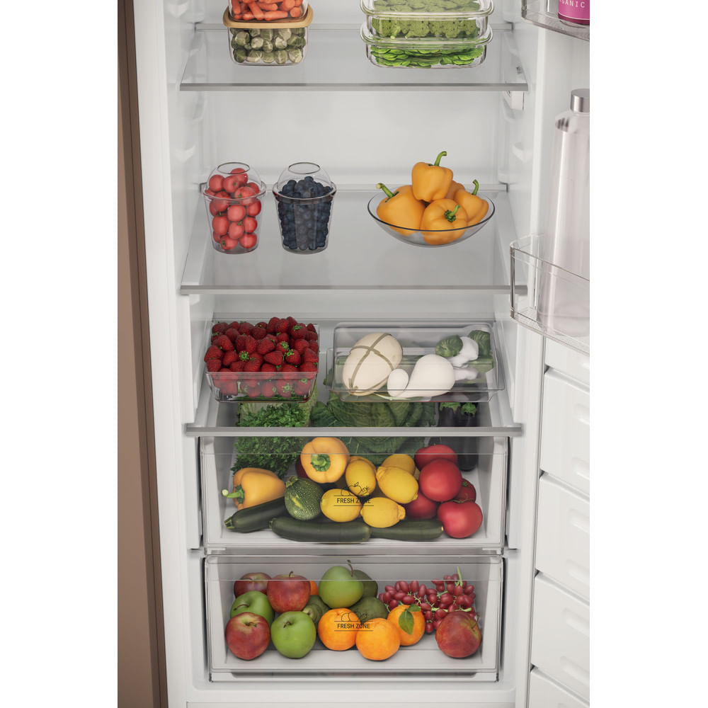 Un frigorifero bianco ben fornito con verdure fresche, frutta in contenitori e ripiani.