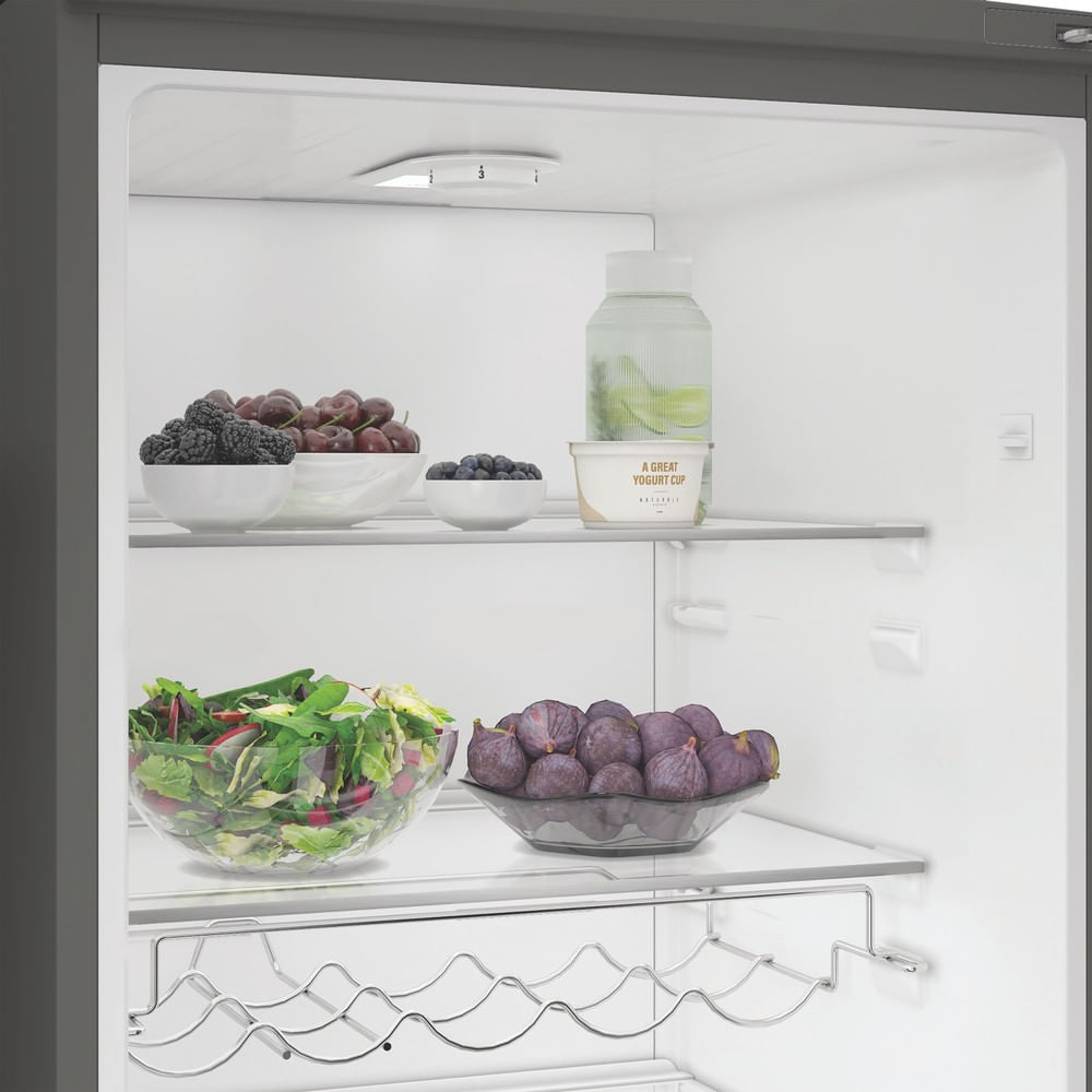 Interno di un frigorifero aperto con frutta fresca, insalata e yogurt sui ripiani.
