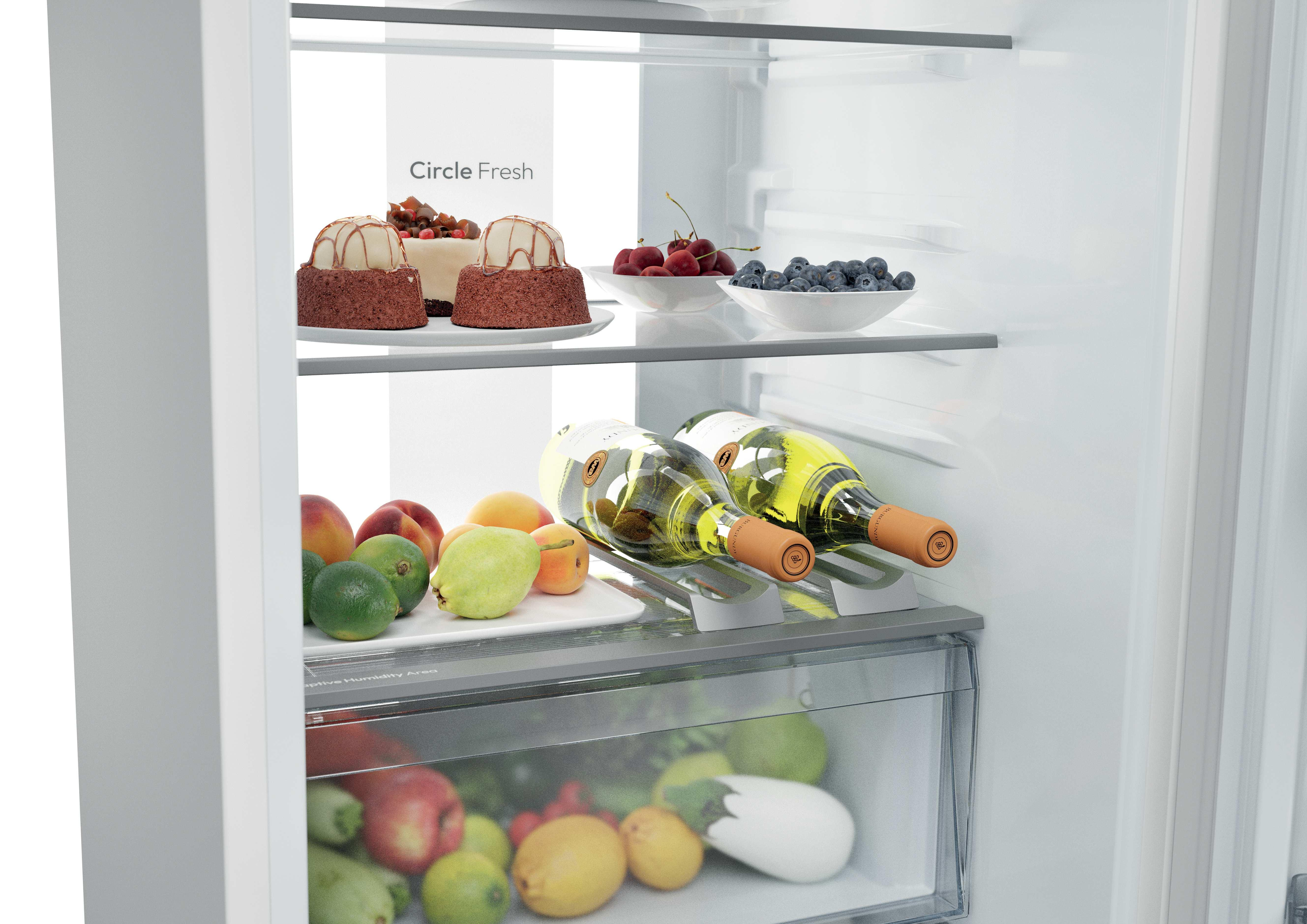 Interno di frigorifero aperto con dessert, frutta fresca, bottiglie di vino e verdure nel cassetto inferiore.
