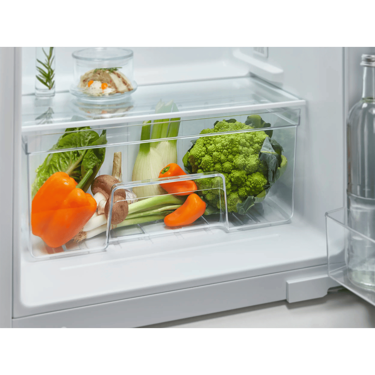 Un frigorifero aperto con verdure fresche nei cassetti trasparenti e cibo sul ripiano in vetro.