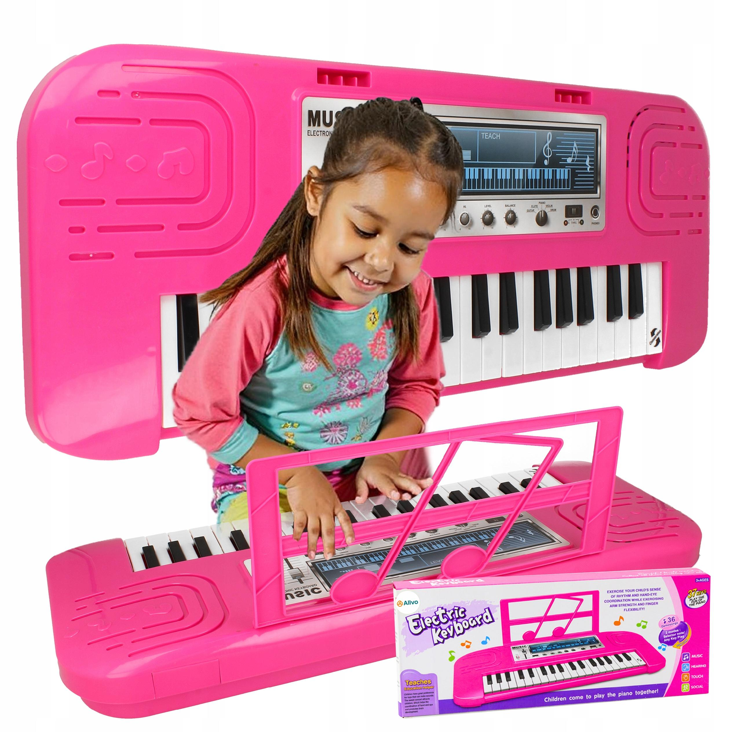 Uśmiechnięta dziewczynka gra na jasnoróżowym elektronicznym keyboardzie-zabawce, obok widoczny jest karton.