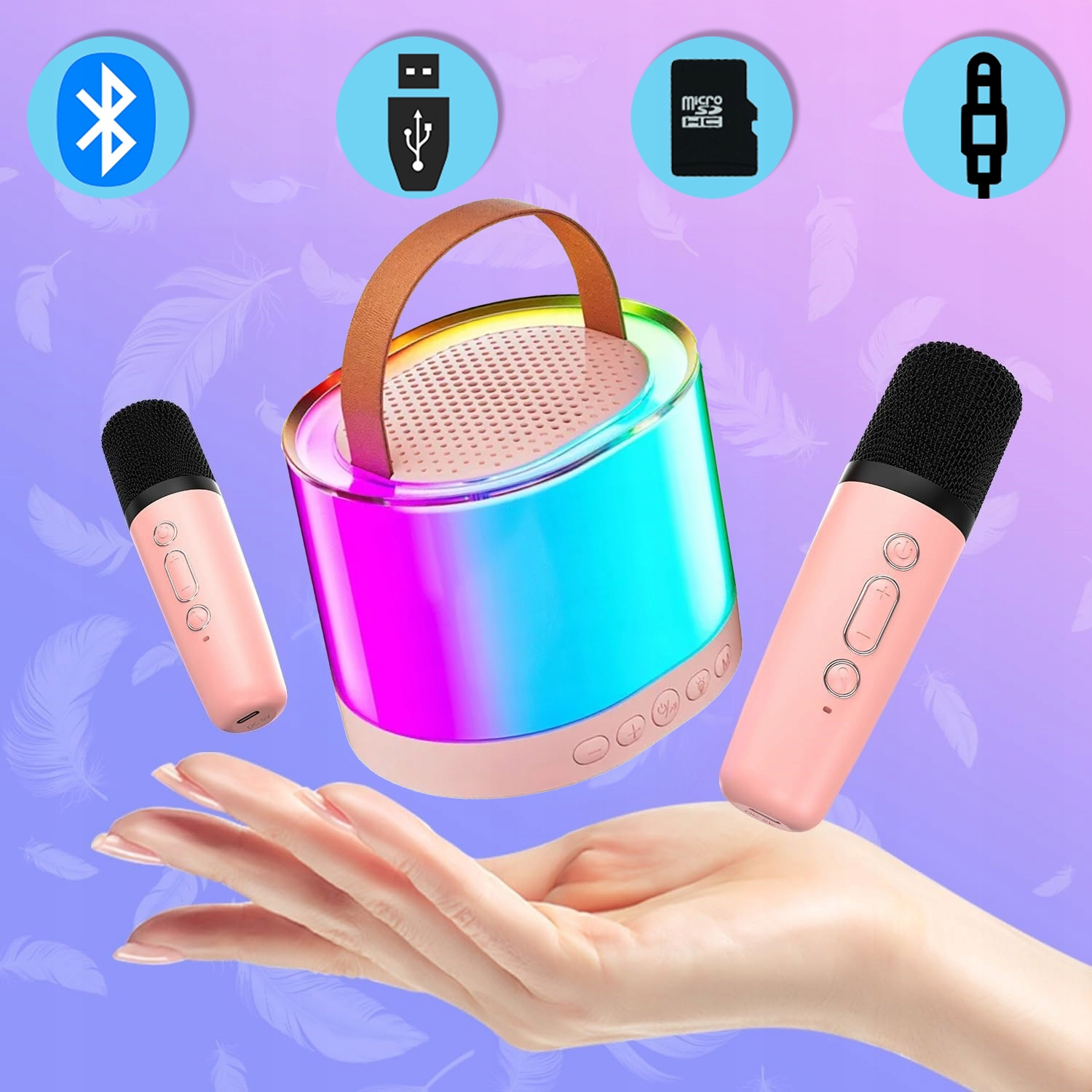 Dłoń trzyma kolorowe urządzenie do karaoke i dwa różowe mikrofony, z ikonami Bluetooth, USB i SD u góry.