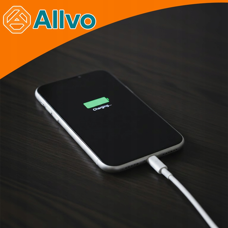 Smartfon ładuje się na ciemnym drewnianym stole za pomocą białego kabla, a w lewym górnym rogu widoczne jest logo Allvo.