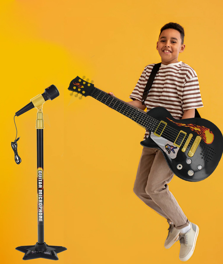 Chłopiec w w paski skacze, trzymając czarną gitarę-zabawkę na żółtym tle, obok stojak z mikrofonem.