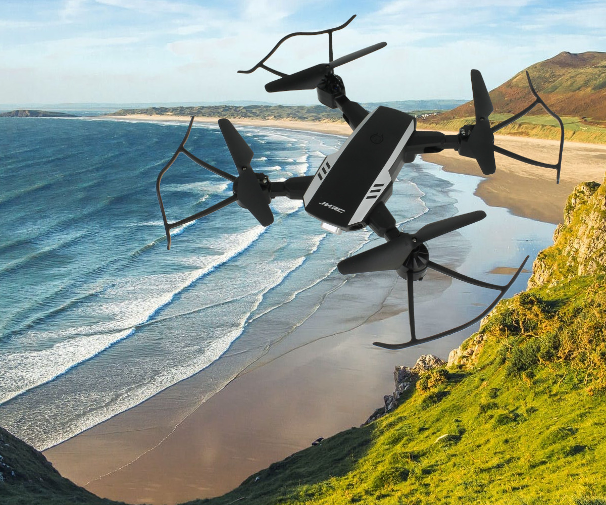 Czarny dron z osłonami śmigieł leci przed nadmorskim krajobrazem z oceanem i klifami.