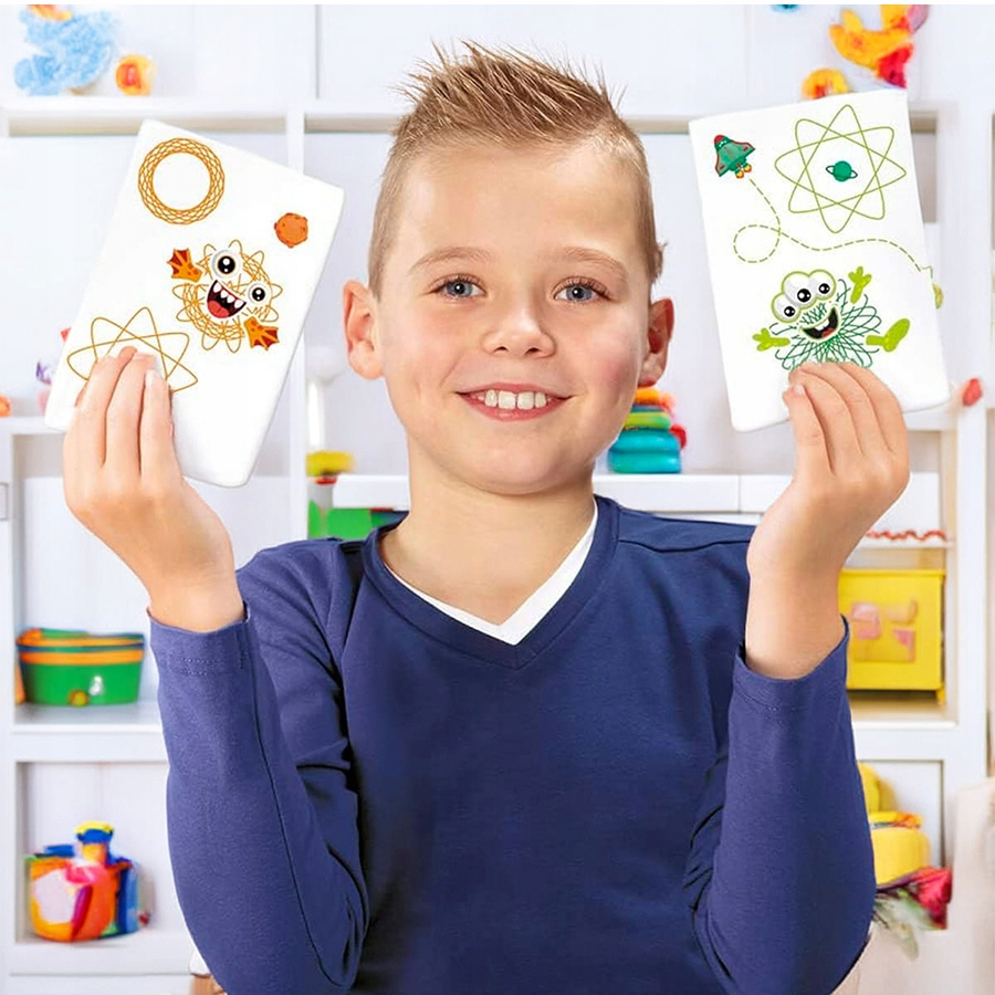 Chłopiec w niebieskim swetrze z uśmiechem trzyma dwie karty z rysunkami kosmosu i potworów.