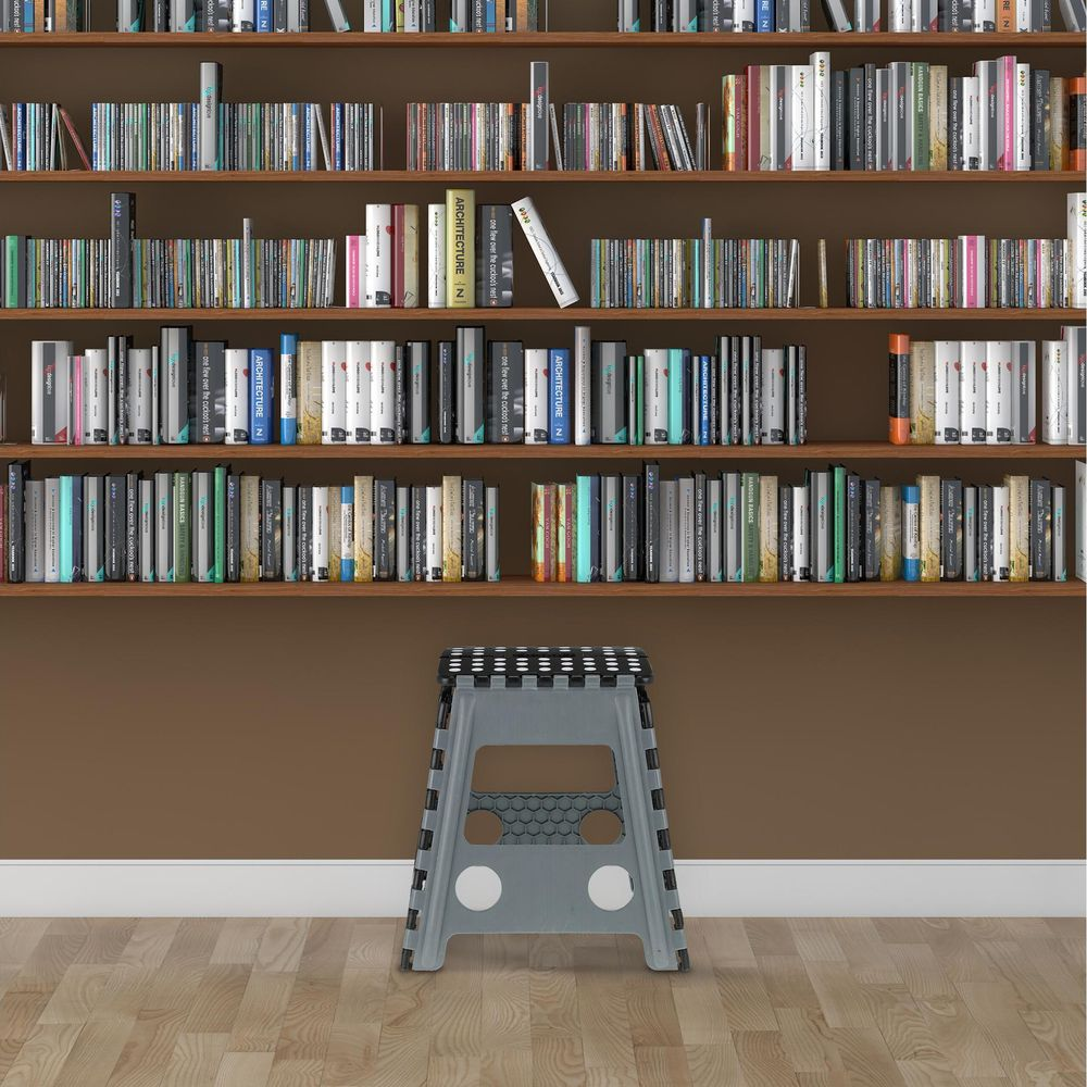 Ein kleiner grauer Klapphocker steht vor einer Wand mit vollen Bücherregalen und Holzboden.
