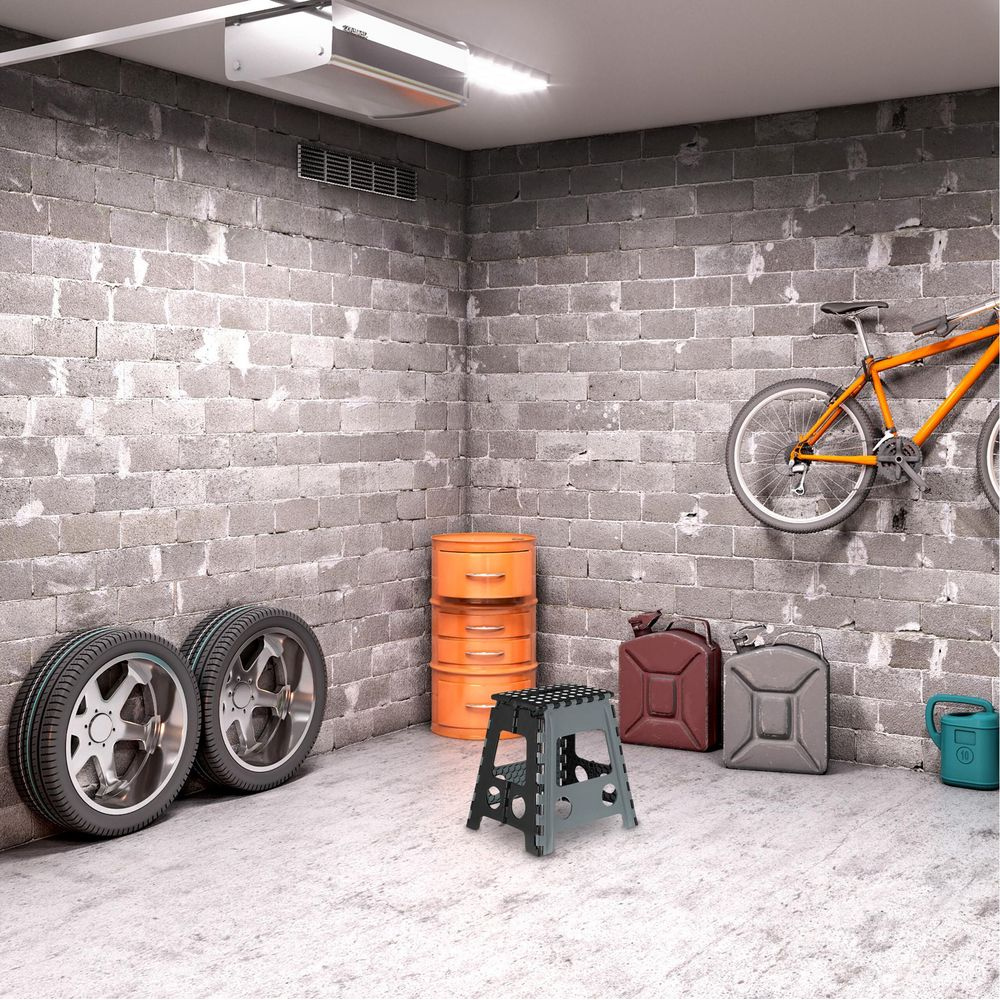 Eine graue Betongaragenecke mit zwei Autoreifen, einem kleinen grauen Hocker, orangefarbenen Schubladen, zwei Kanistern und einem orangen Fahrrad.