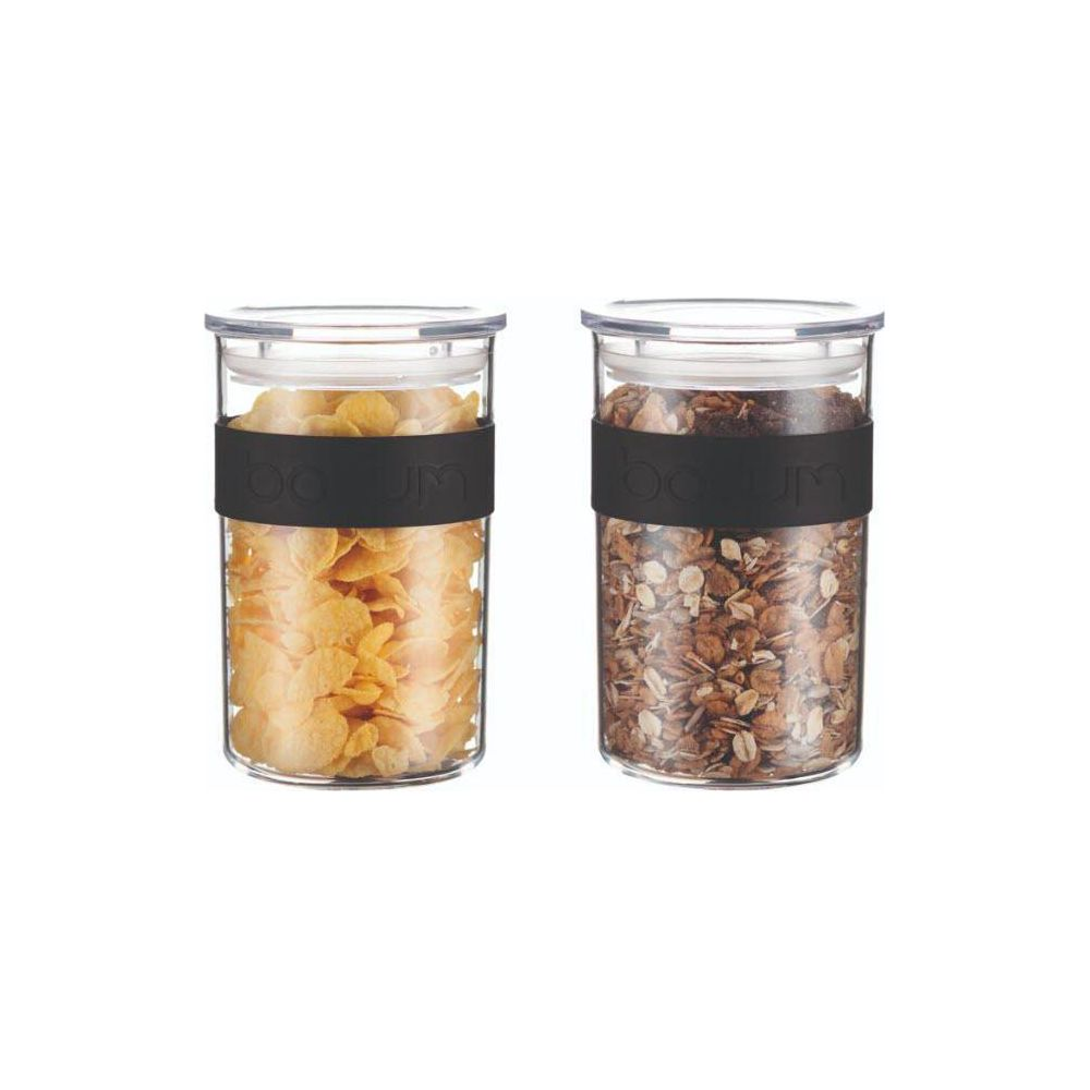 Zwei klare Glasbehälter mit schwarzen Silikonbändern, gefüllt mit gelben Cornflakes und Müsli auf weißem Hintergrund.