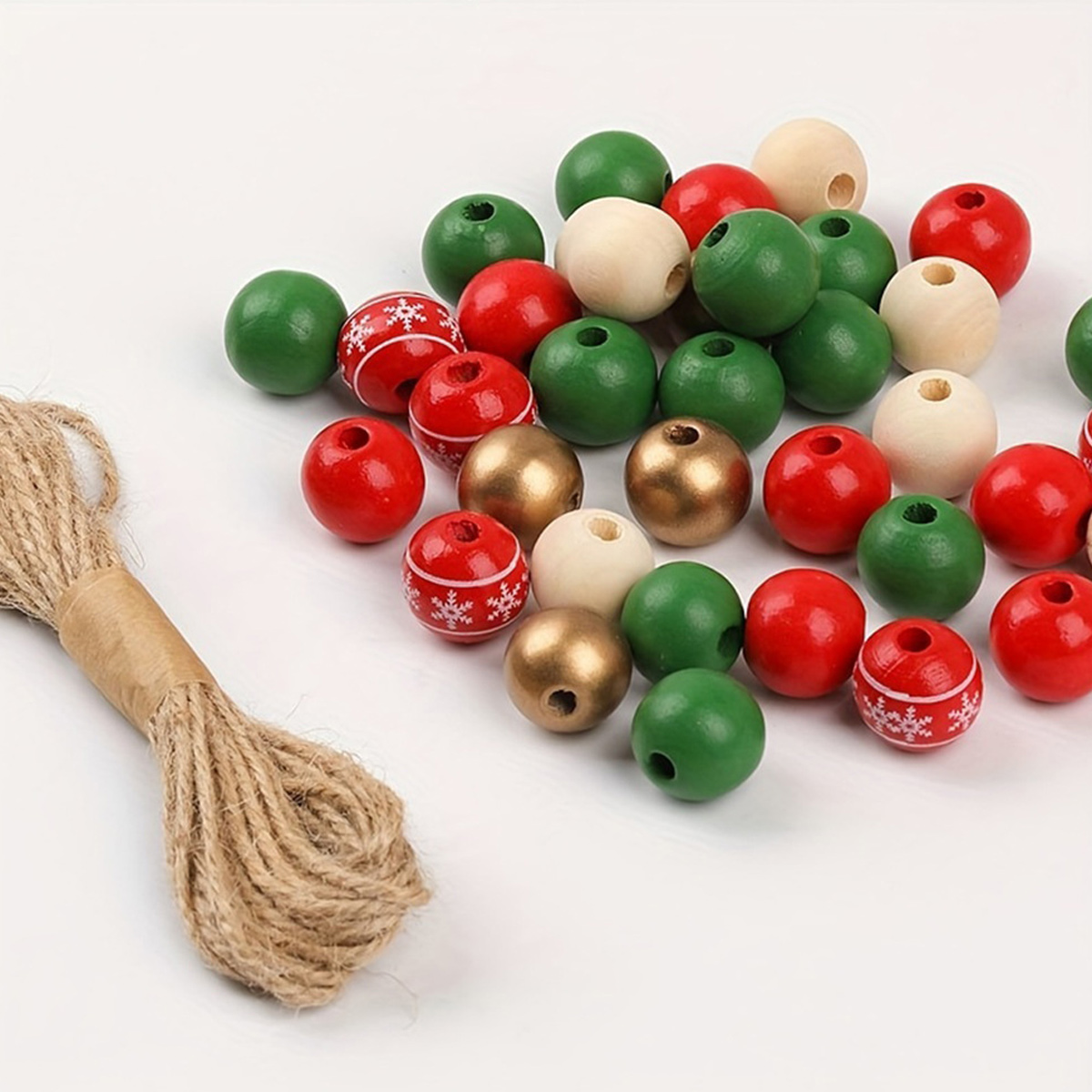Eine Ansammlung von roten, grünen, goldenen und naturfarbenen Holzperlen neben einem Bündel Juteschnur auf weißem Hintergrund.