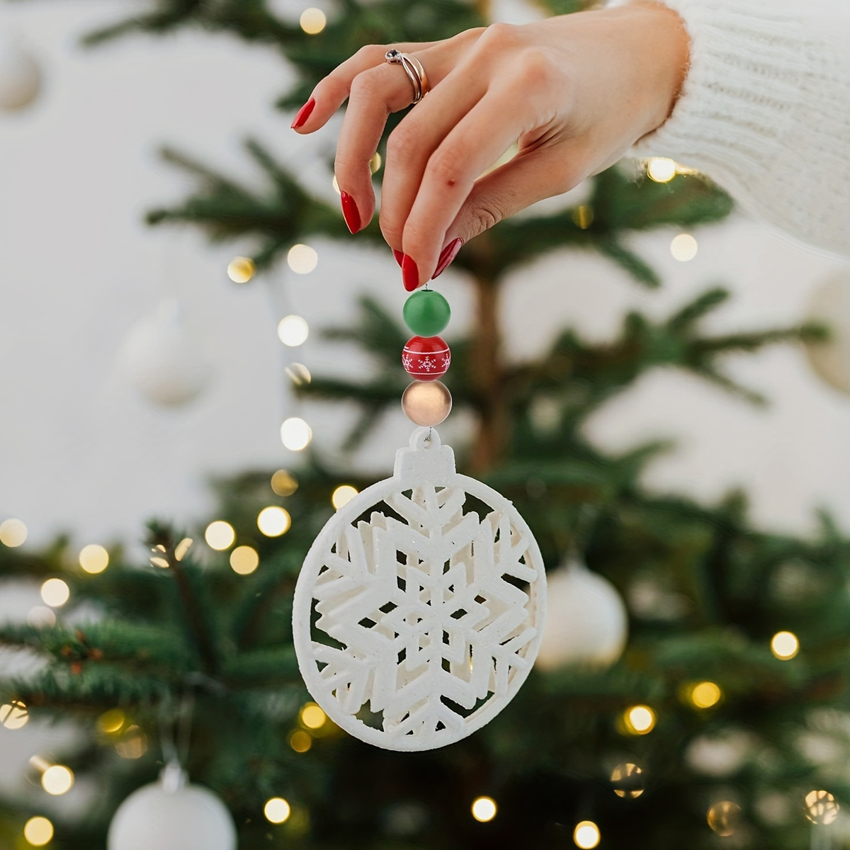 Eine Hand hält eine weiße Schneeflocken-Weihnachtskugel vor einem geschmückten Baum.