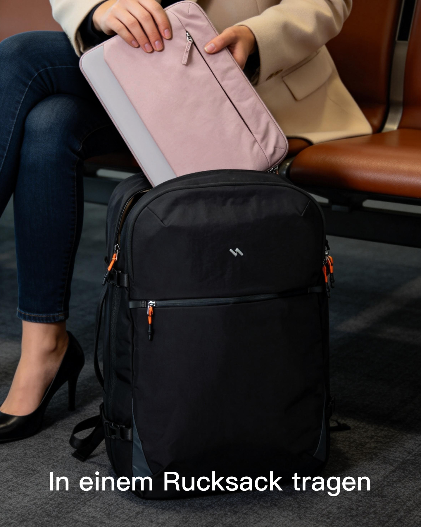 Eine Frau in einem beigen Mantel und blauen Jeans legt eine rosa Laptoptasche in einen schwarzen Rucksack.
