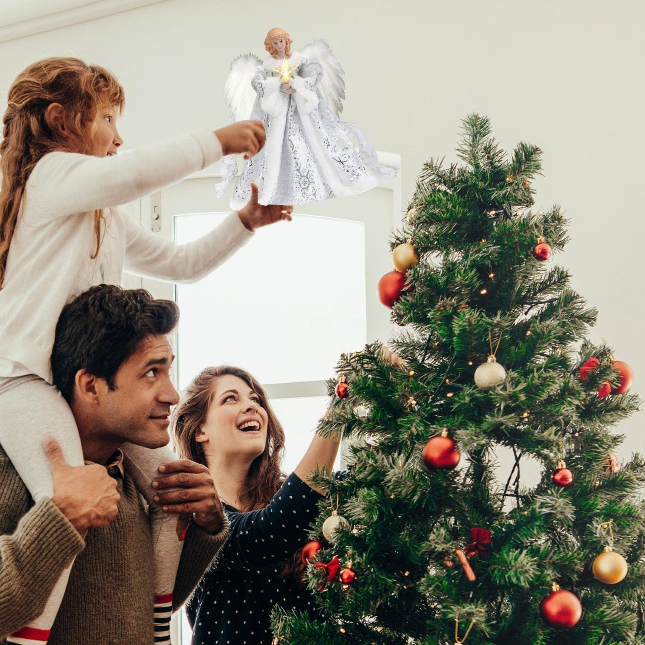 Eine Familie platziert gemeinsam einen leuchtenden Weihnachtsengel auf der Baumspitze.