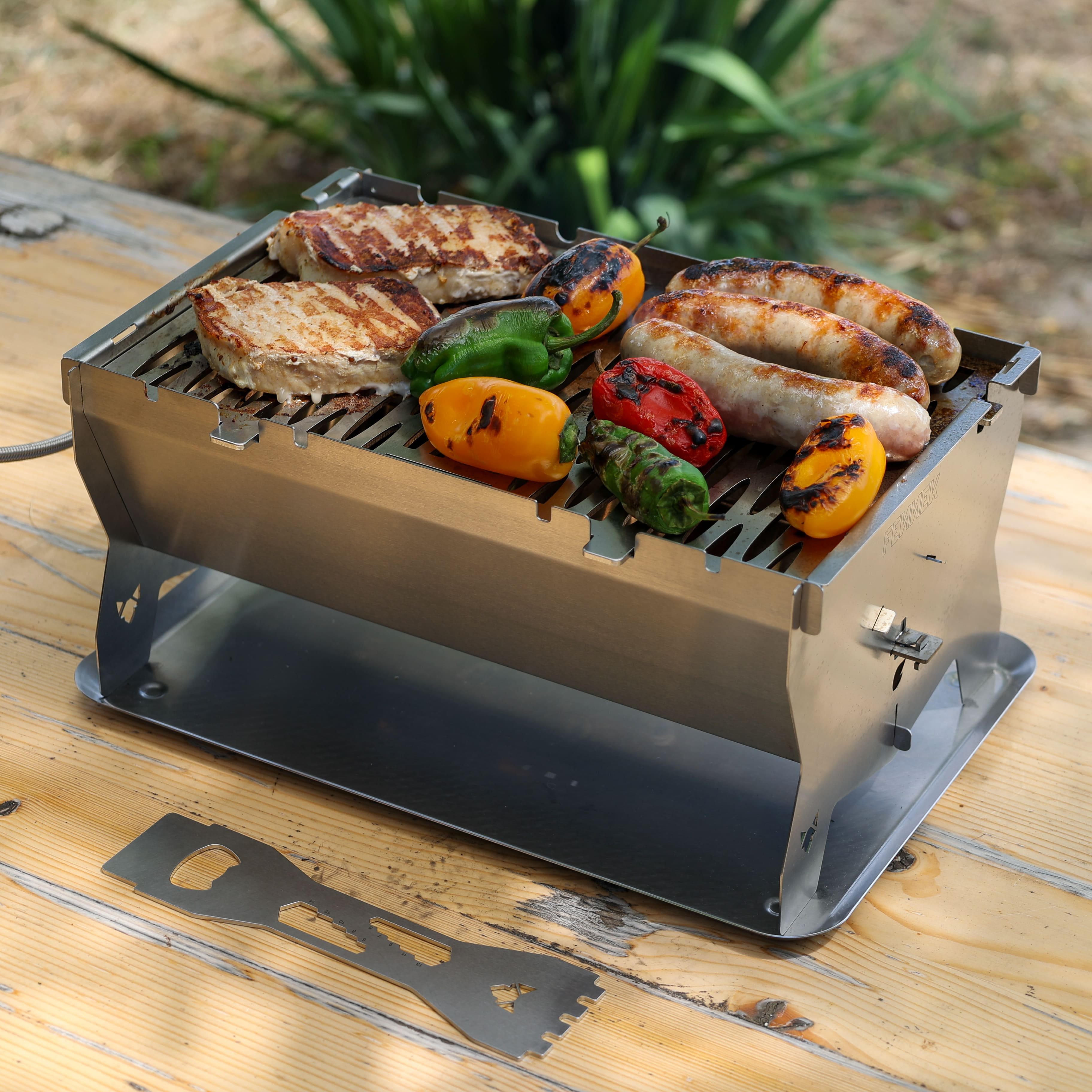 Kleiner Grill auf Holz Tisch mit Steaks, Würstchen und bunten Paprika.