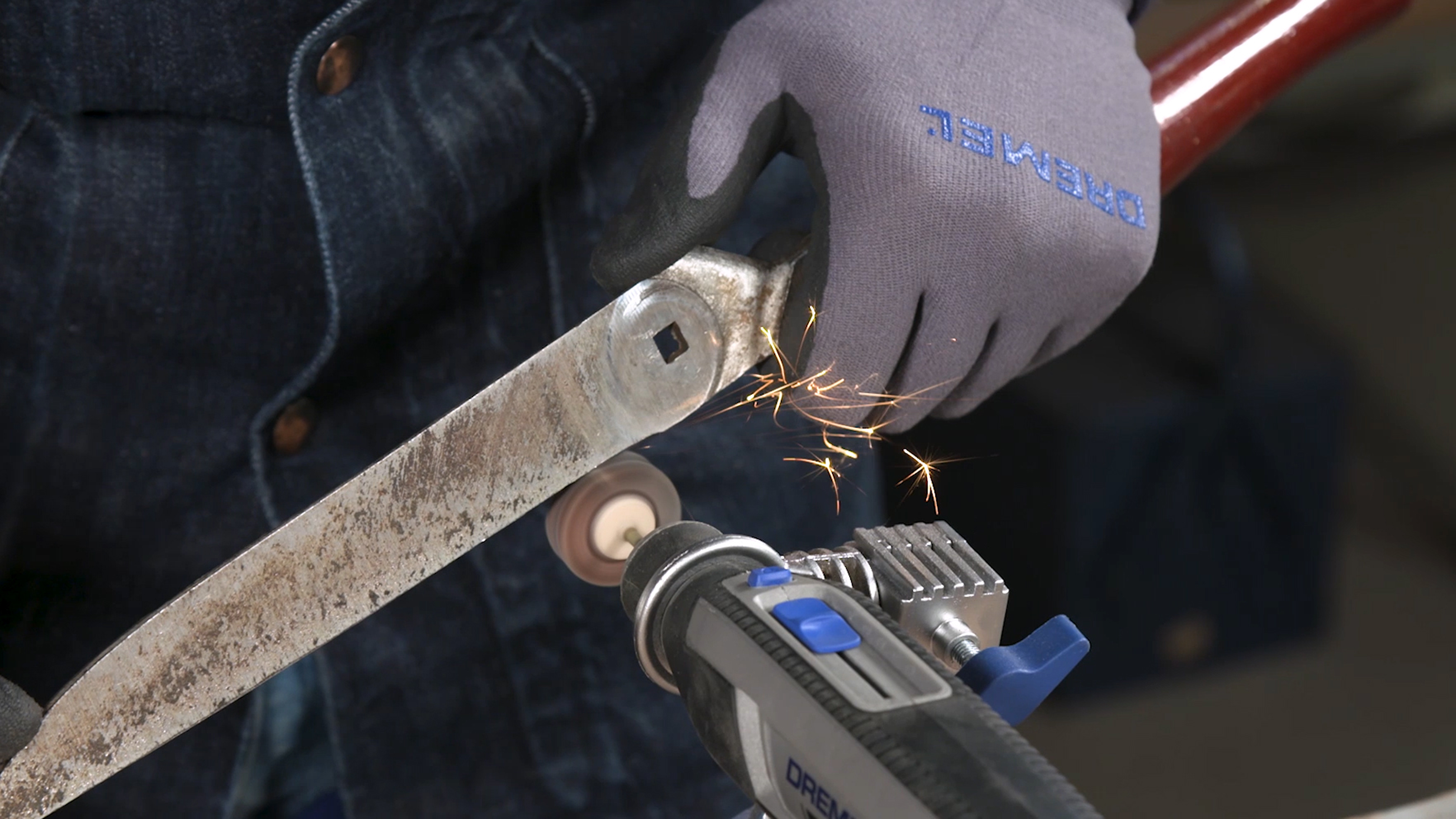 Eine behandschuhte Hand hält ein Metallwerkzeug gegen ein Dremel-Multifunktionswerkzeug.