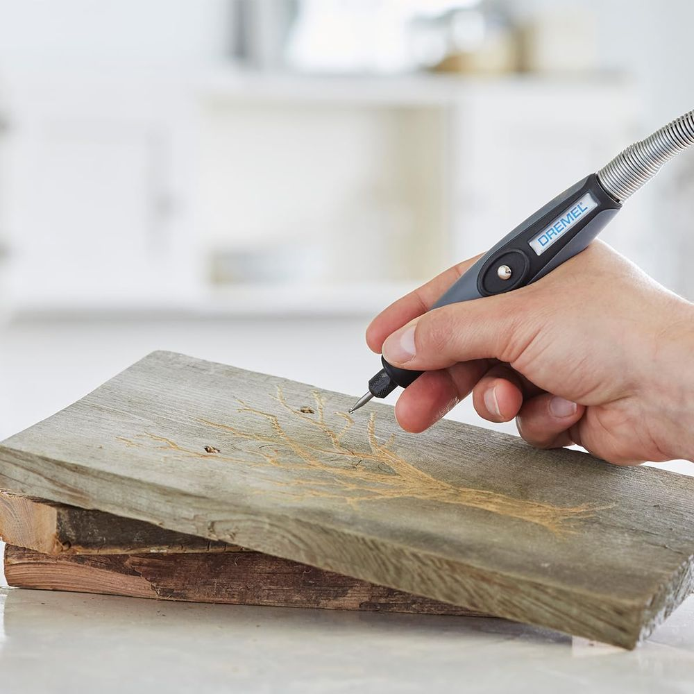 Eine Hand hält ein Dremel-Werkzeug und graviert ein Baummotiv in ein Holzstück.