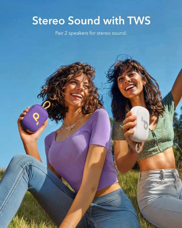 Due donne sorridenti sedute all'aperto sull'erba tengono piccoli altoparlanti portatili.