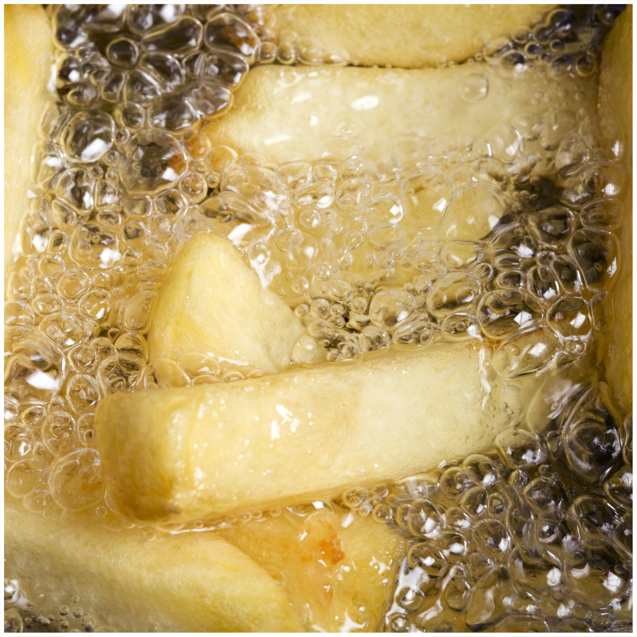 Golden-brown french fries are deep frying in bubbling hot oil with many small bubbles.
