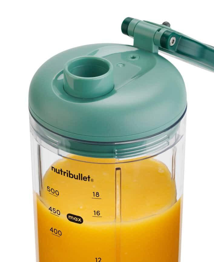 Green Nutribullet cup filled with yellow juice and measurement markings on a white background.