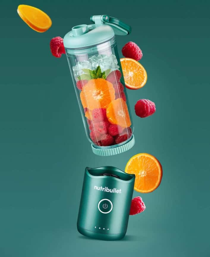 Portable Nutribullet blender with floating raspberries, oranges, and ice.